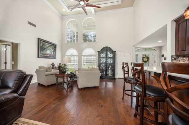 living area with visible vents, crown molding, dark wood-style flooring, a towering ceiling, and ceiling fan