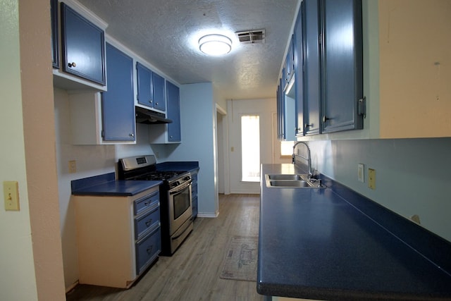 kitchen featuring wood-type flooring, sink, blue cabinetry, stainless steel gas range, and a textured ceiling