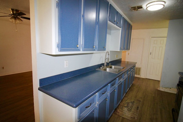 kitchen with sink, dark wood-type flooring, blue cabinetry, ceiling fan, and a textured ceiling