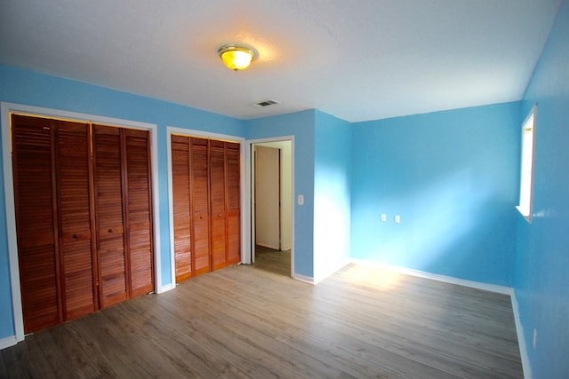 unfurnished bedroom featuring multiple closets and wood-type flooring