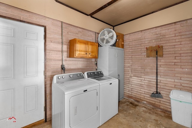 clothes washing area featuring cabinets, separate washer and dryer, and brick wall