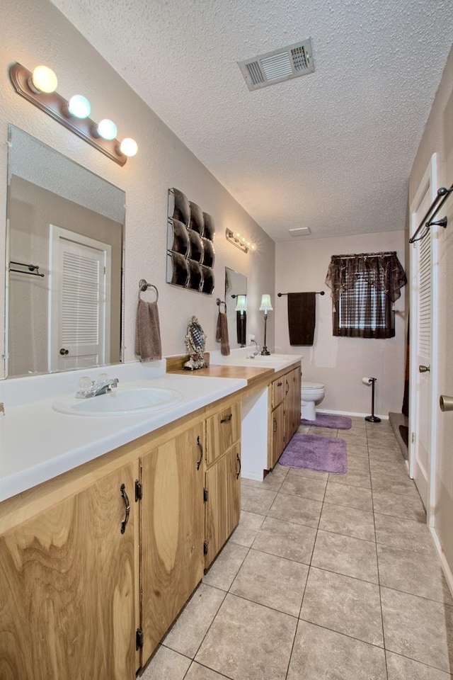 bathroom featuring tile patterned flooring, vanity, a textured ceiling, and toilet