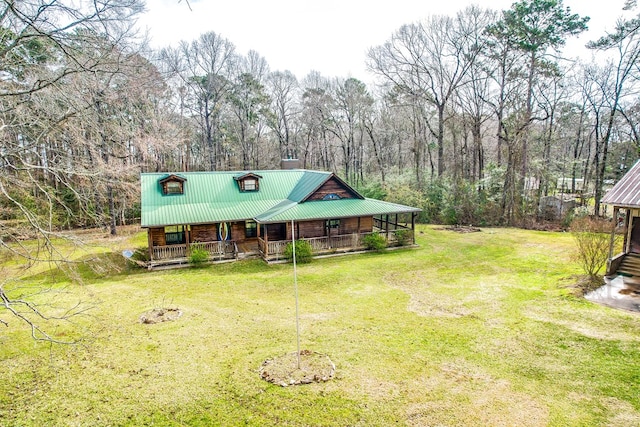 view of front facade with a front lawn, a wooded view, covered porch, and metal roof