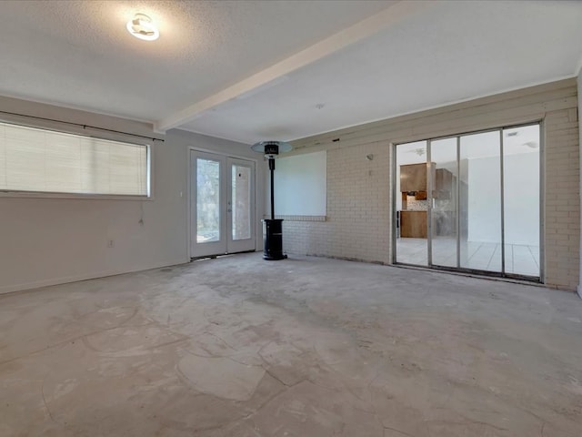 empty room with beamed ceiling, a textured ceiling, brick wall, and unfinished concrete floors