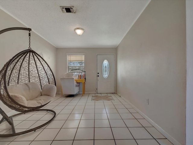 foyer featuring light tile patterned floors, a textured ceiling, visible vents, baseboards, and ornamental molding