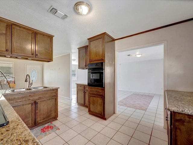 kitchen featuring brown cabinets, light tile patterned floors, visible vents, a sink, and black oven