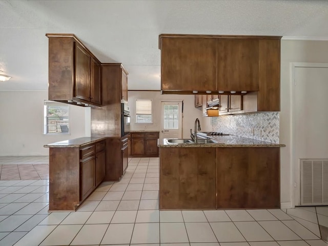 kitchen with a sink, a peninsula, wall oven, and visible vents