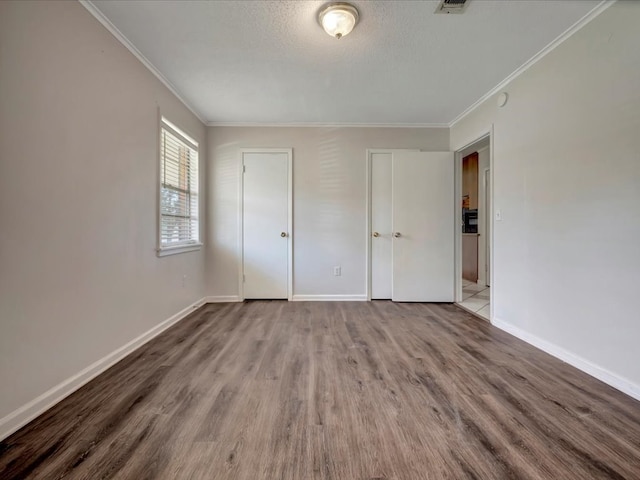 unfurnished bedroom featuring crown molding, a textured ceiling, baseboards, and wood finished floors