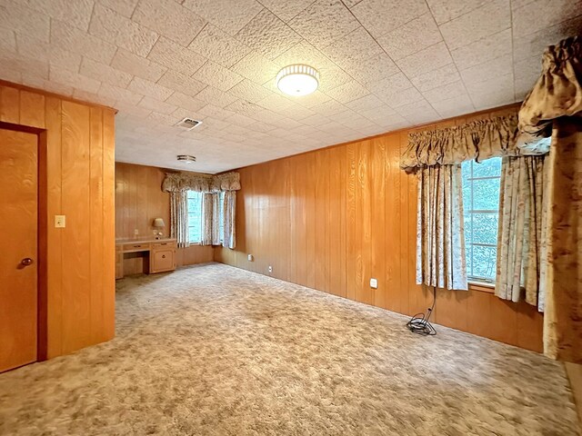 carpeted empty room featuring visible vents and wood walls