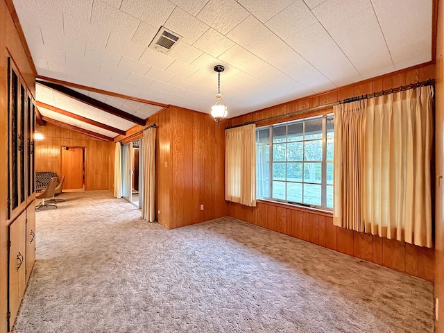 carpeted spare room featuring lofted ceiling with beams, visible vents, and wood walls