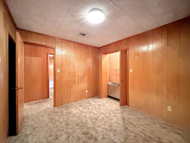 unfurnished bedroom featuring wooden walls, carpet, and visible vents
