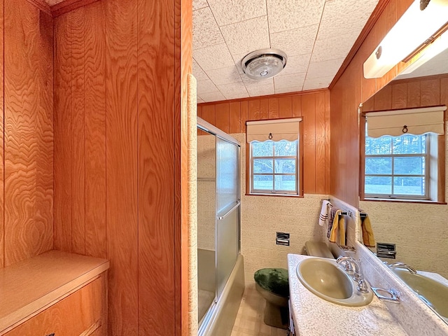 full bathroom featuring vanity, bath / shower combo with glass door, wood walls, crown molding, and tile walls