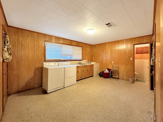 clothes washing area with visible vents, separate washer and dryer, cabinet space, a sink, and wood walls