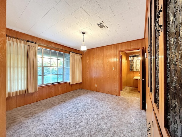 carpeted spare room with visible vents and wood walls