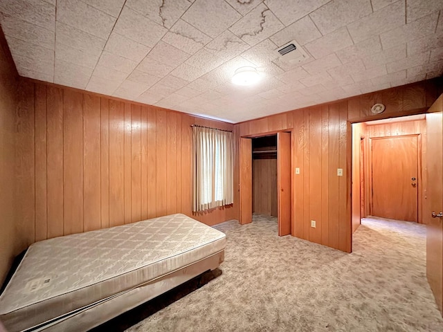unfurnished bedroom featuring a closet, wooden walls, visible vents, and carpet flooring