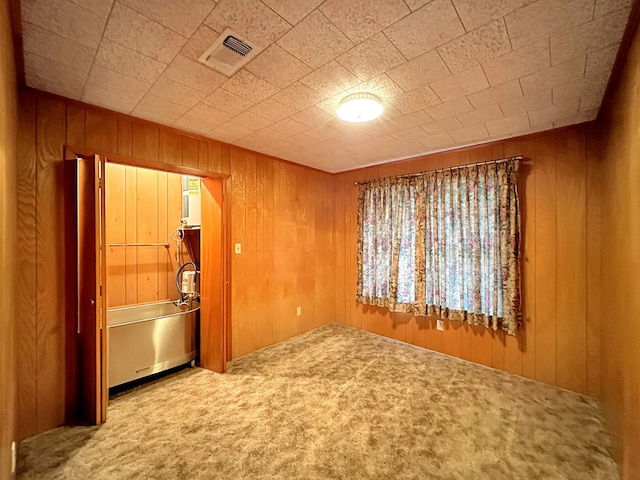 spare room with carpet flooring, visible vents, and wood walls