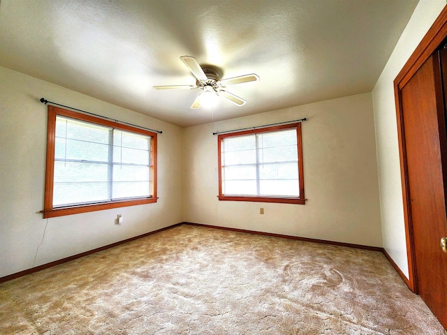 spare room featuring baseboards, plenty of natural light, light colored carpet, and ceiling fan