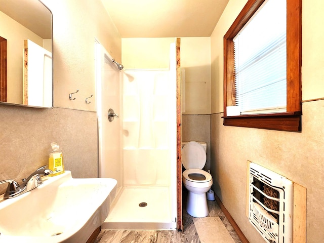 bathroom featuring toilet, heating unit, a stall shower, and a sink