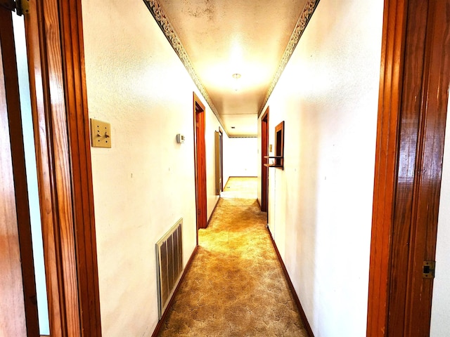 hallway with light carpet, a textured ceiling, and ornamental molding