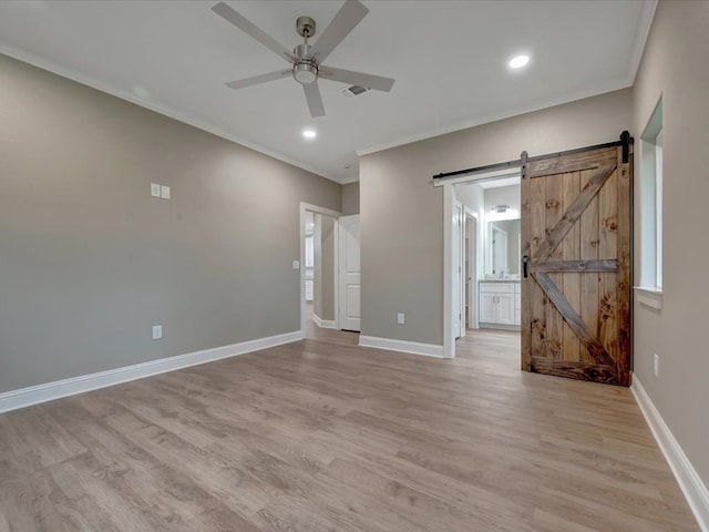 unfurnished room with light wood-style flooring, a ceiling fan, crown molding, baseboards, and a barn door