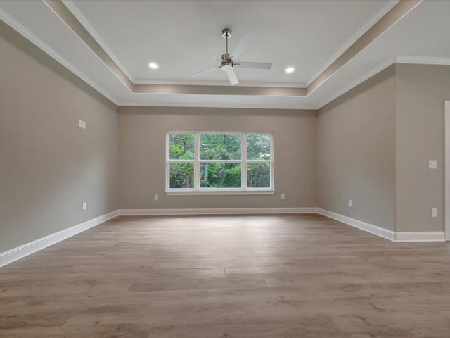 spare room with ceiling fan, crown molding, light wood finished floors, a tray ceiling, and baseboards