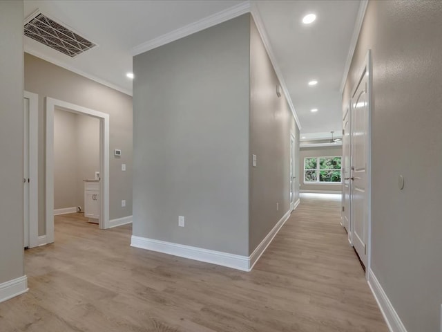 hallway featuring light wood-type flooring, ornamental molding, visible vents, and baseboards