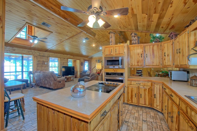 kitchen with a center island, wooden ceiling, wooden walls, appliances with stainless steel finishes, and tile counters