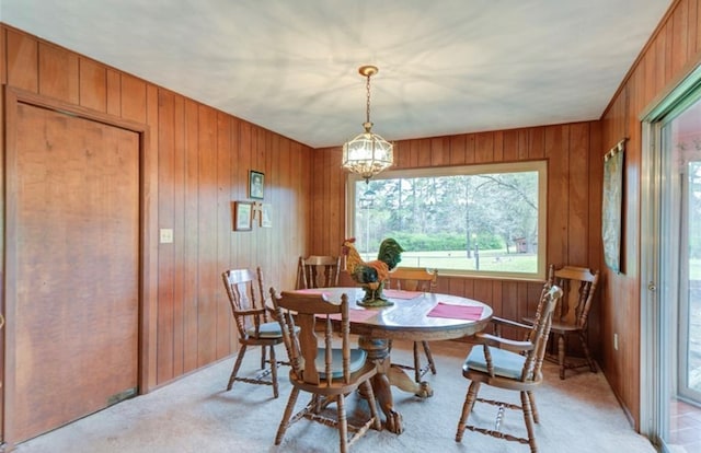 dining room featuring a chandelier, wood walls, and light carpet