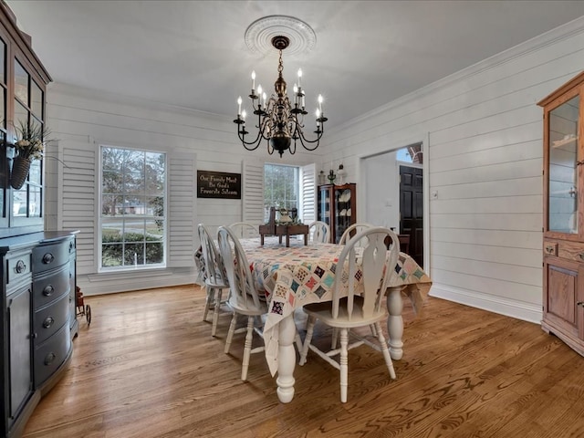 dining area featuring light hardwood / wood-style floors, wooden walls, and a chandelier