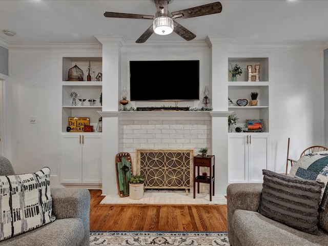 living room featuring built in shelves, ceiling fan, crown molding, light hardwood / wood-style flooring, and a fireplace