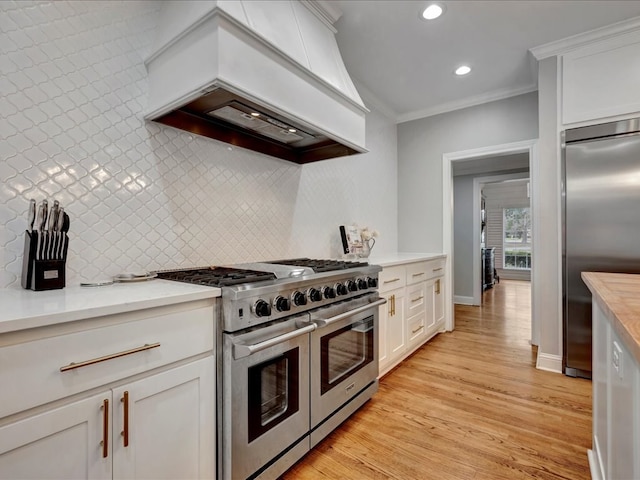 kitchen with white cabinets, high end appliances, custom range hood, and ornamental molding