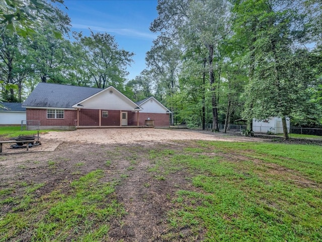 rear view of property featuring a yard, brick siding, an outdoor fire pit, and fence