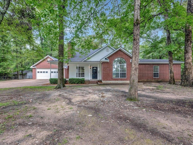 ranch-style home with driveway, covered porch, a garage, brick siding, and a chimney