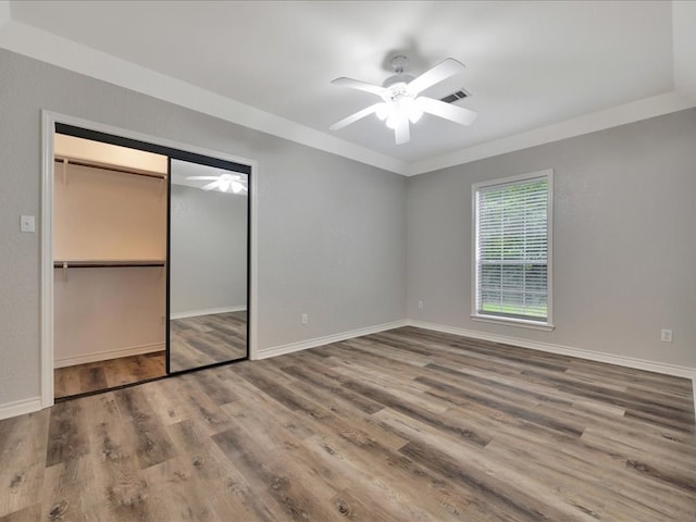 unfurnished bedroom featuring wood-type flooring, a closet, crown molding, and ceiling fan