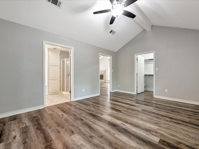 unfurnished bedroom with a spacious closet, visible vents, vaulted ceiling with beams, and wood finished floors