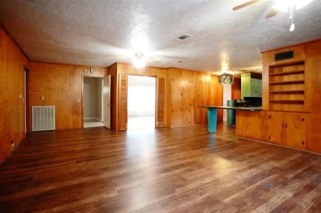 unfurnished living room featuring built in shelves, wood walls, dark hardwood / wood-style flooring, and a textured ceiling