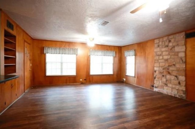 empty room featuring a textured ceiling, dark hardwood / wood-style flooring, built in features, and wooden walls