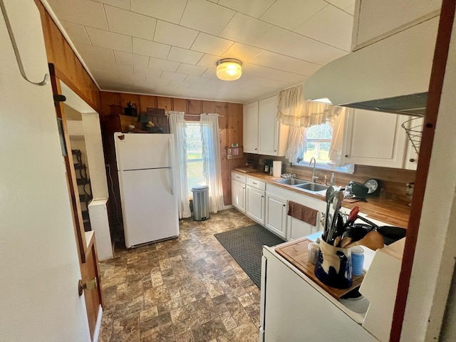 kitchen with wood walls, sink, range hood, white fridge, and white cabinetry