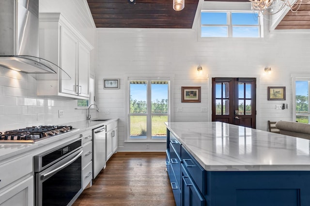 kitchen with a wealth of natural light, stainless steel appliances, wall chimney range hood, blue cabinets, and white cabinets