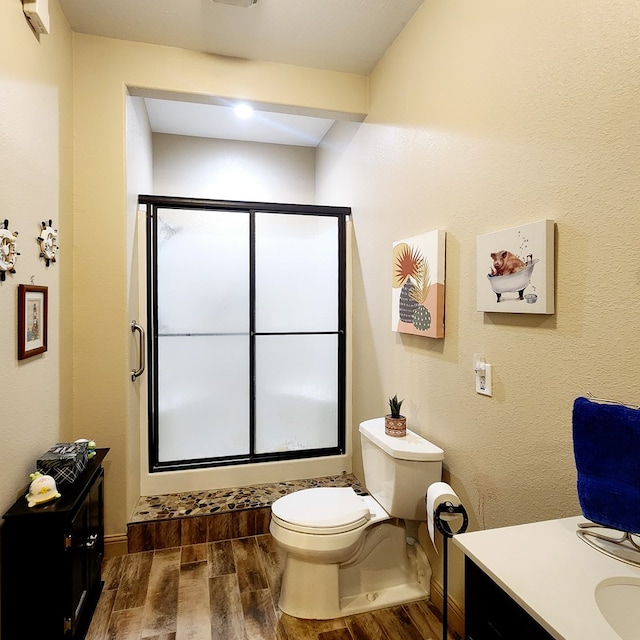 bathroom featuring toilet, wood finished floors, a stall shower, vanity, and baseboards