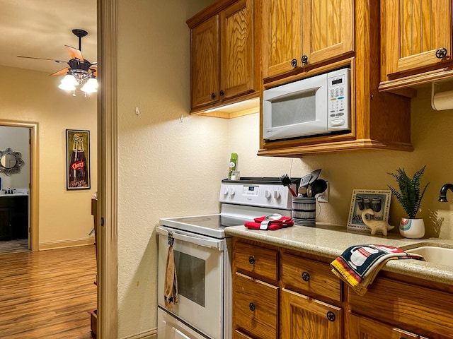 kitchen with brown cabinets, light countertops, wood finished floors, a ceiling fan, and white appliances