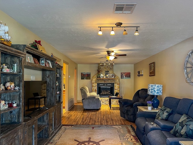 living area featuring visible vents, a fireplace, light wood-style flooring, a textured ceiling, and ceiling fan