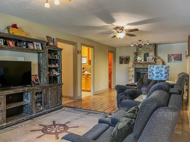 living area featuring rail lighting, a ceiling fan, wood finished floors, and a fireplace