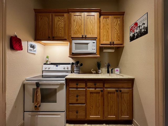 kitchen featuring light countertops, brown cabinetry, a sink, and white appliances