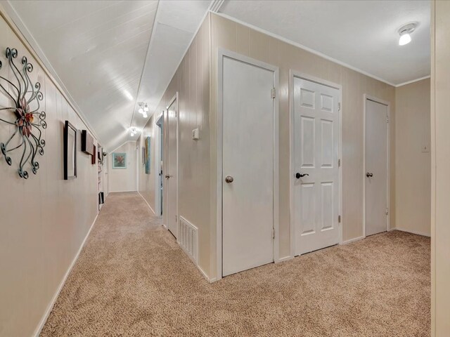 hallway with crown molding, wood walls, light colored carpet, and vaulted ceiling