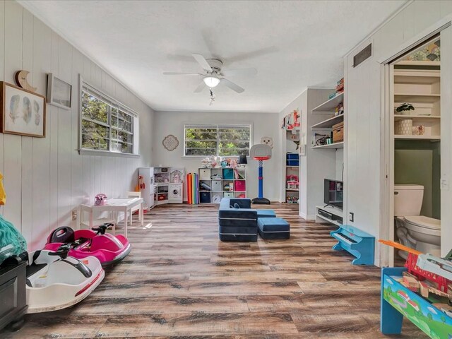 recreation room with wood-type flooring, ceiling fan, and wood walls