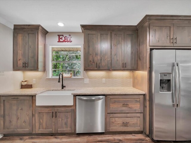 kitchen with sink, appliances with stainless steel finishes, tasteful backsplash, light stone counters, and wood-type flooring