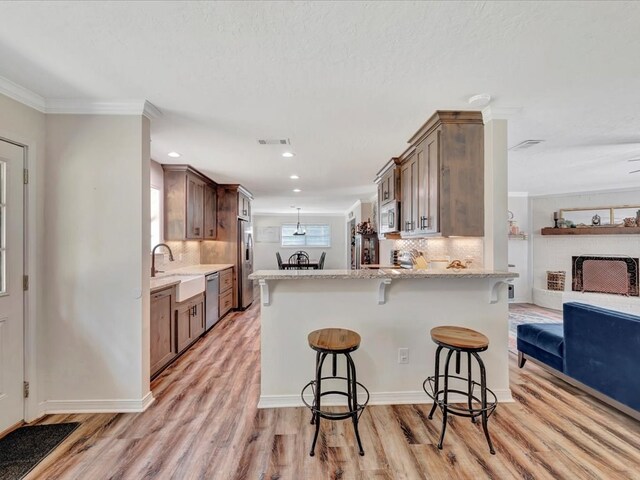 kitchen with kitchen peninsula, stainless steel appliances, crown molding, light hardwood / wood-style flooring, and a breakfast bar area