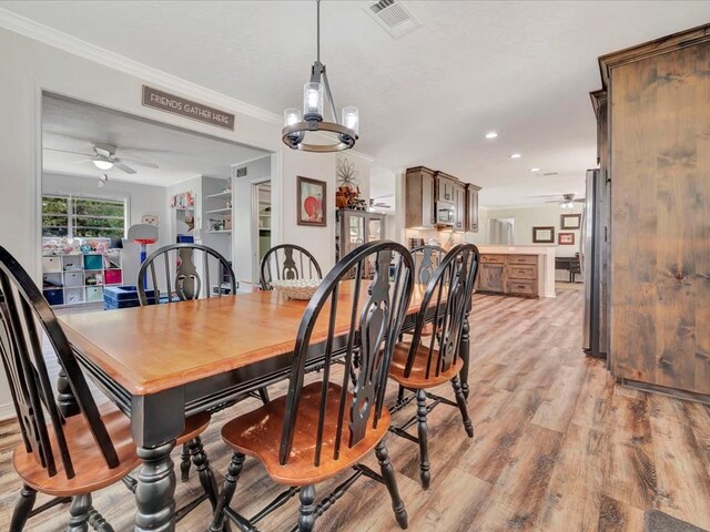 dining room featuring ceiling fan with notable chandelier, a textured ceiling, light wood-type flooring, and crown molding