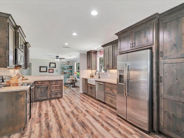 kitchen featuring kitchen peninsula, appliances with stainless steel finishes, dark brown cabinetry, and light hardwood / wood-style flooring